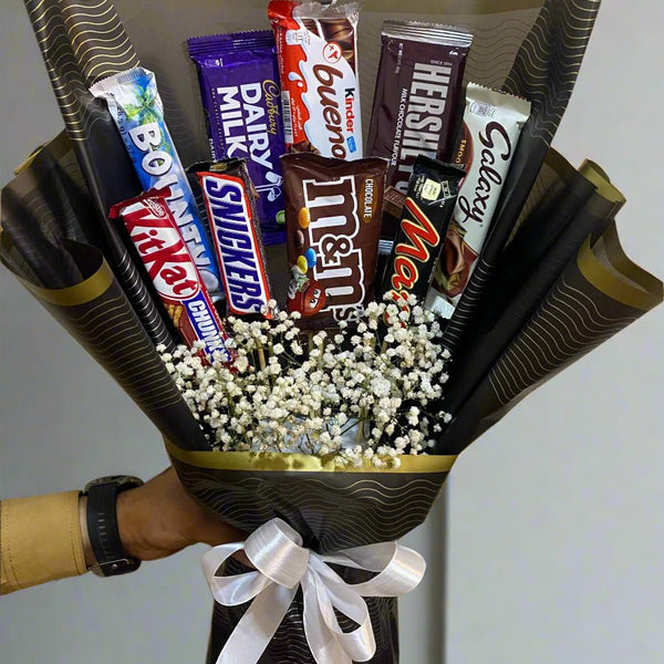 A bouquet of chocolate bars arranged in a V-shape with baby's breath flowers, wrapped with black paper and tied with a white ribbon.